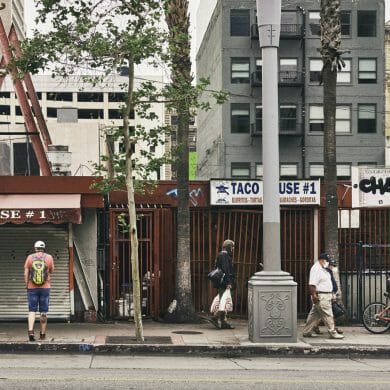 Pedestrians in downtown Los Angeles walk in front of closed storefronts.