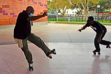 Two adult men balance mid-motion on their roller skates at an outdoor park.