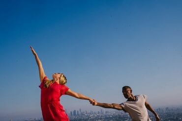 Two people dance against the backdrop of a blue sky and the L.A. skyline.