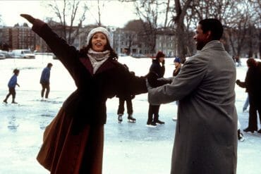 A woman and man ice skate together on a frozen outdoor lake.