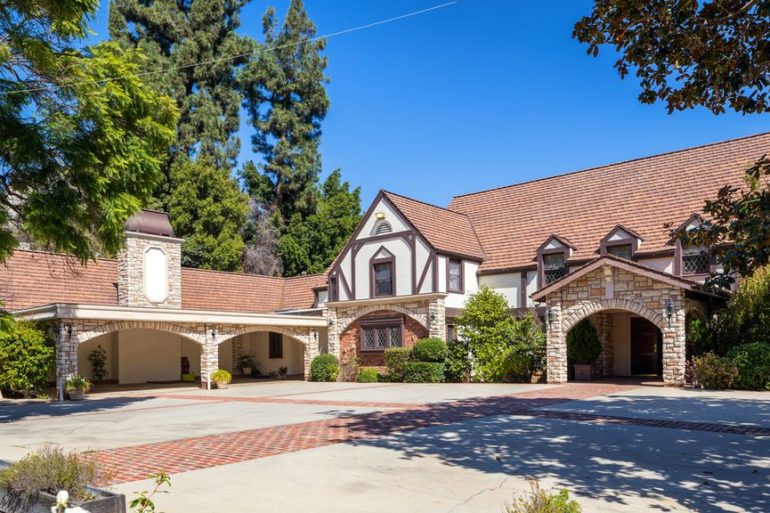 The driveway leading to the front of a large home surrounded by trees.