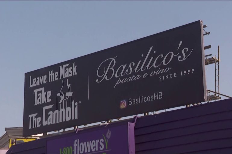 A billboard reading: "Leave the Mask Take the Cannoli," a puppet master illustration from the film "The Godfather" and Basilico's Pasta e Vino's restaurant information.