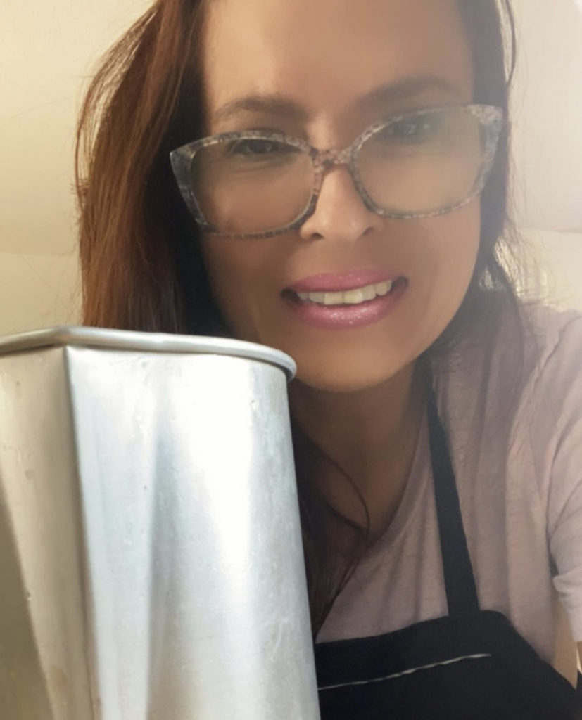 A woman smiles at the camera, wearing an apron and holding a pitcher.