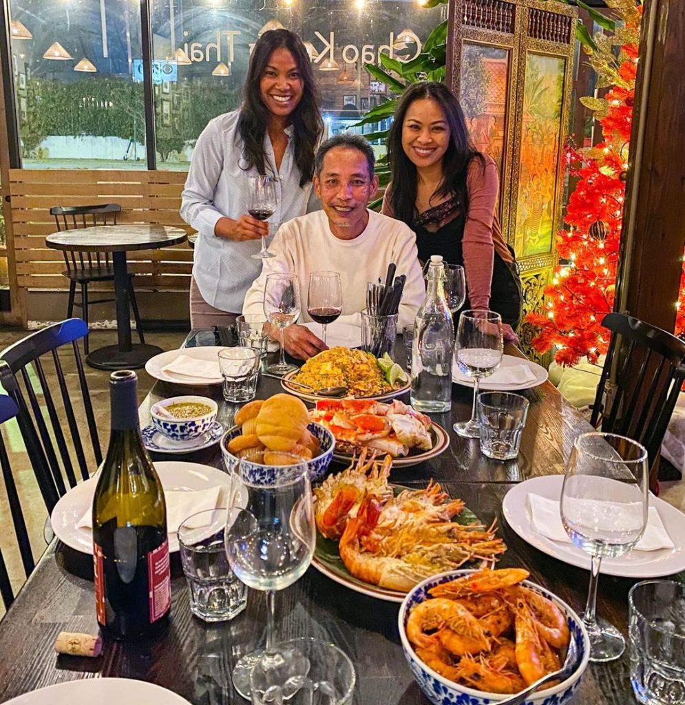 Three people sit at the end of a restaurant dining table, smiling.